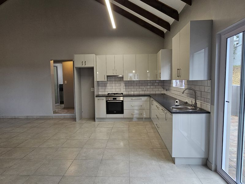 Spacious open-plan kitchen and living area featuring vaulted ceilings with exposed timber beams, modern cabinetry, and direct access to an outdoor patio.