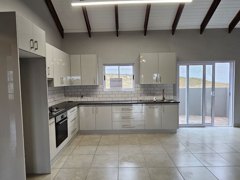 Modern open-plan kitchen featuring high-gloss cabinetry, subway tile backsplash, and exposed timber beams, leading out to a patio area.