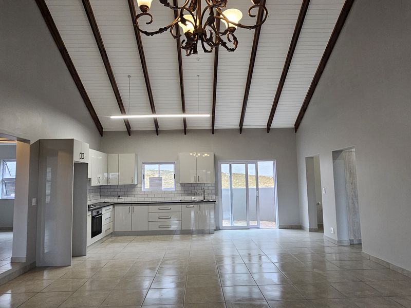 Spacious open-plan living and kitchen area featuring high vaulted ceilings with exposed beams, modern cabinetry, and direct access to the outdoor space.