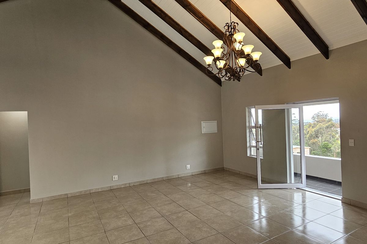 Spacious living area featuring vaulted ceilings with exposed timber beams, tiled flooring, and direct access to a balcony through glass doors.