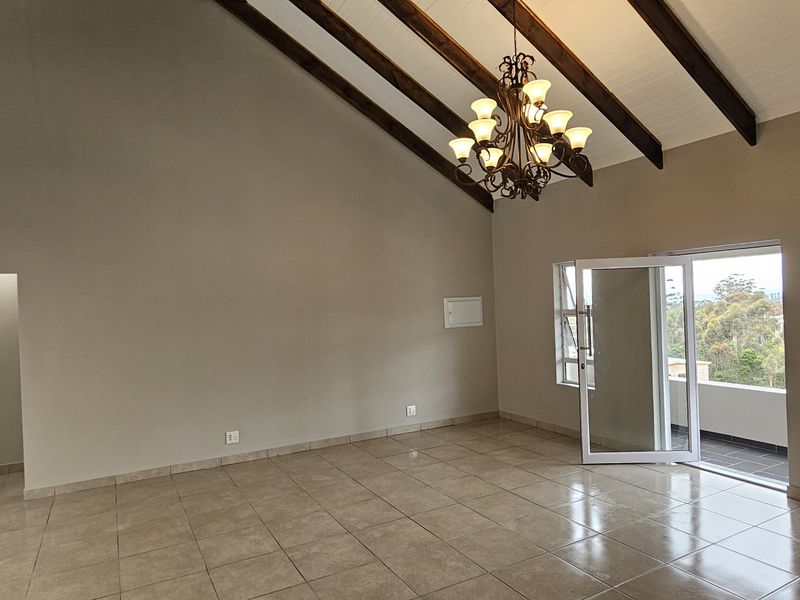 Spacious living area featuring vaulted ceilings with exposed timber beams, tiled flooring, and direct access to a balcony through glass doors.