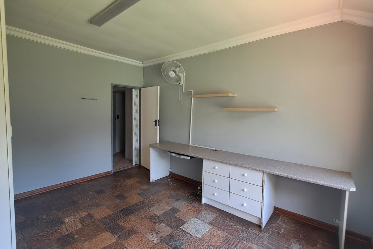 A bedroom featuring built-in desk cabinetry, wall-mounted shelving, and a ceiling fan, offering a functional space with neutral wall tones.