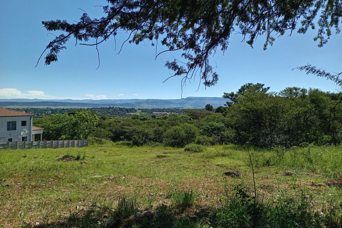 A scenic view overlooking a vacant residential plot with established trees and distant mountain landscape.