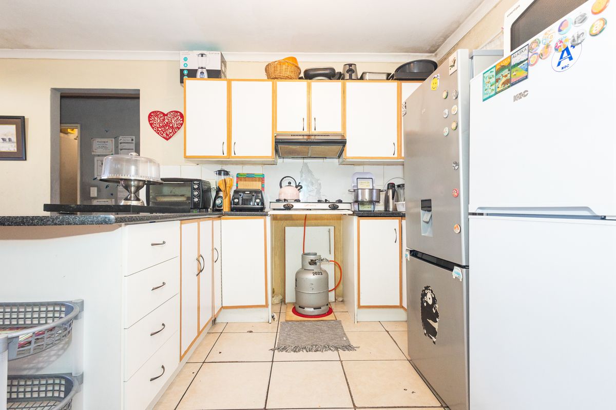 A compact kitchen featuring white cabinetry, tiled flooring, and a gas hob with an extractor fan, requiring some cosmetic updates to improve functionality and aesthetics.