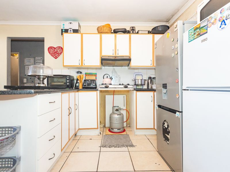 A compact kitchen featuring white cabinetry, tiled flooring, and a gas hob with an extractor fan, requiring some cosmetic updates to improve functionality and aesthetics.