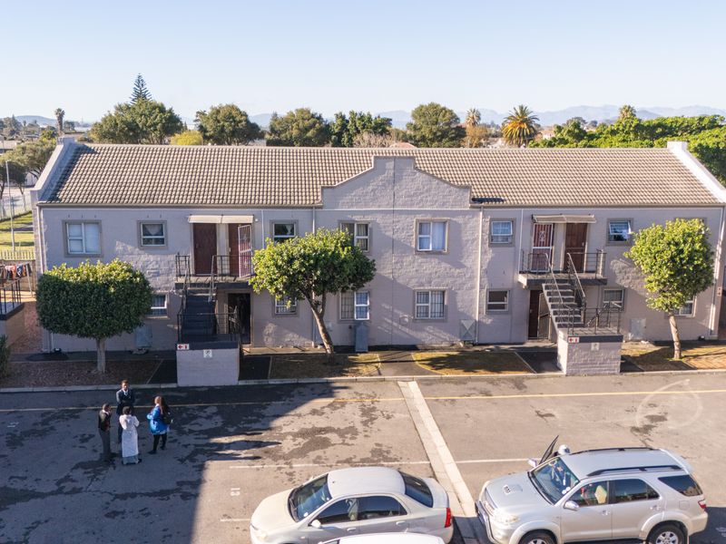 Aerial view of a multi-unit apartment complex featuring a tiled roof, brick facade, and external staircases with an adjacent asphalt parking area.