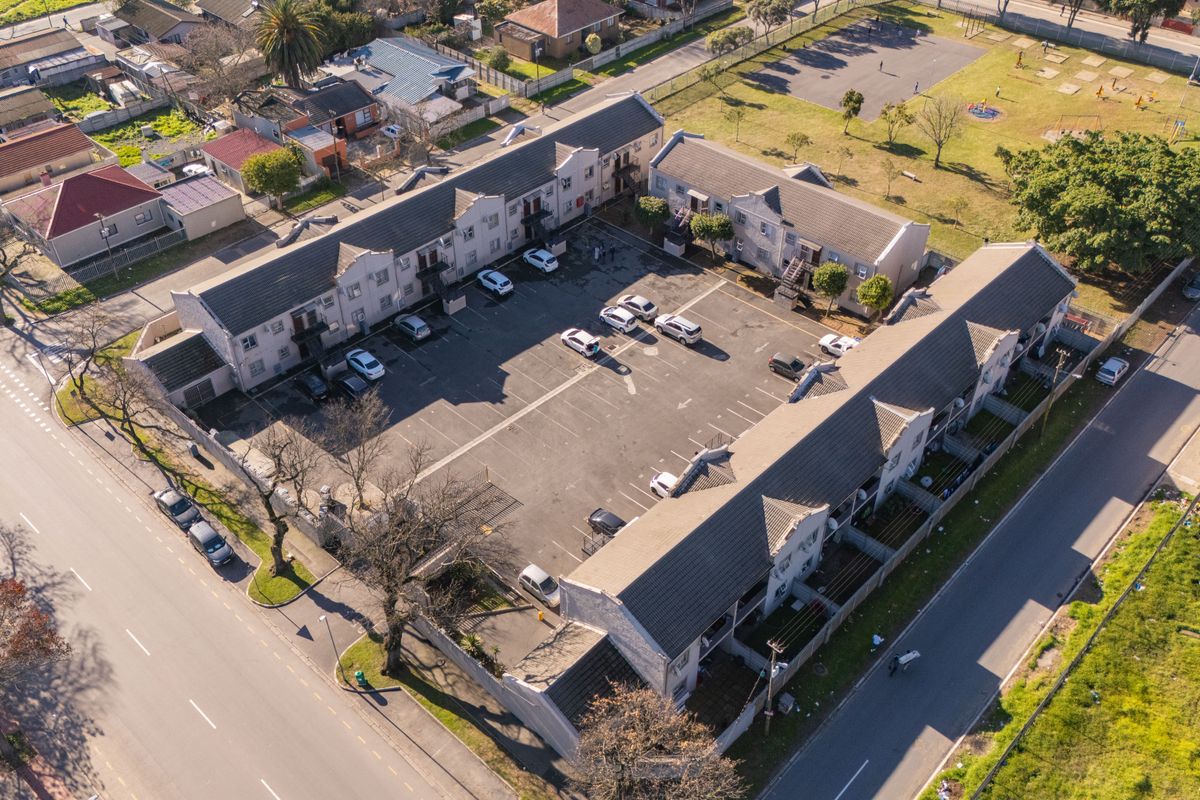 Aerial view of an apartment complex featuring multiple residential blocks, a central paved parking area, and surrounding neighborhood infrastructure.