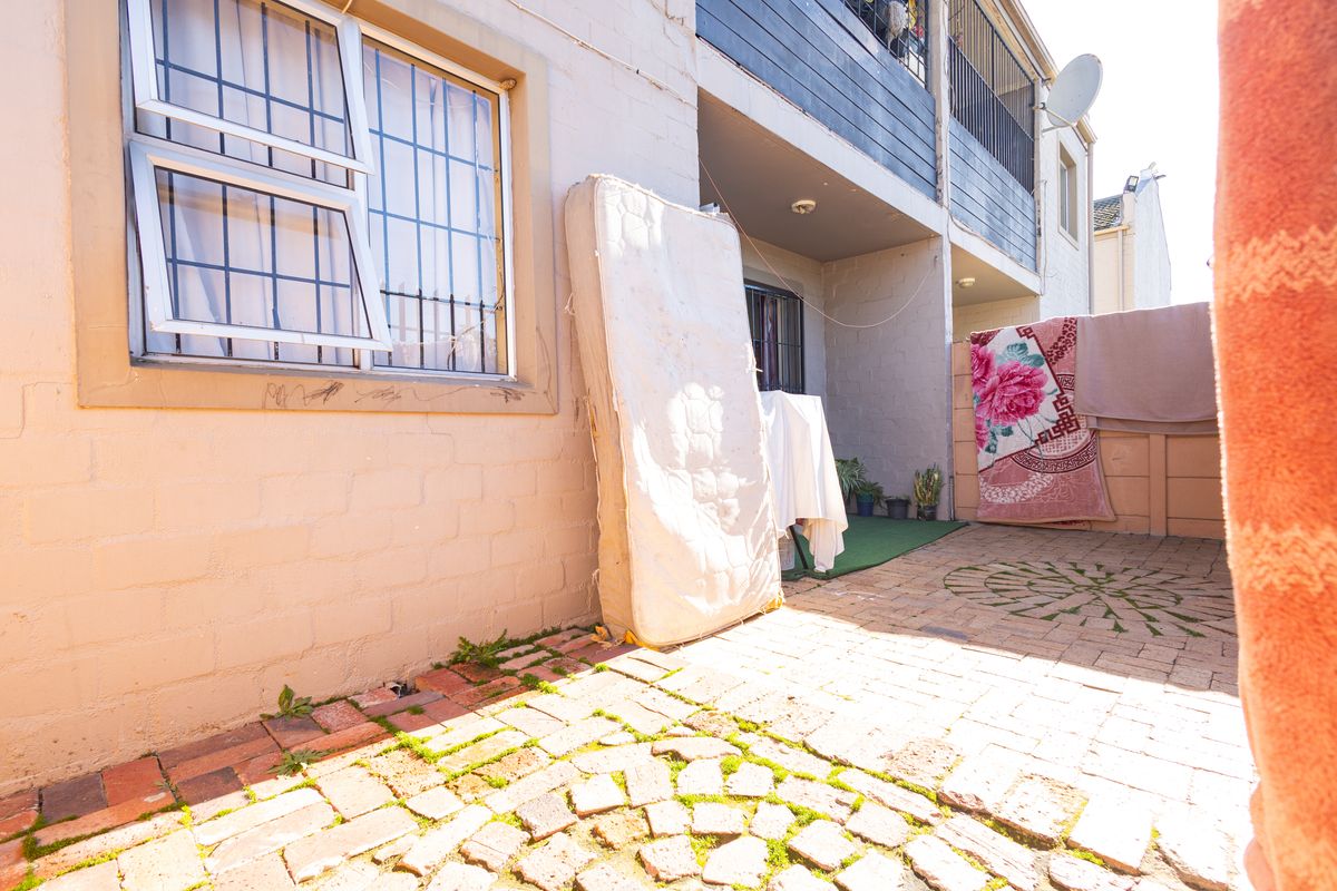 Rear exterior area featuring a paved patio, security bars on windows, and access to an upper-level balcony.