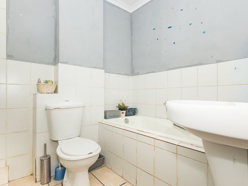 A functional bathroom featuring a standard toilet, bathtub, and pedestal sink with tiled surfaces and unfinished wall areas requiring cosmetic attention.