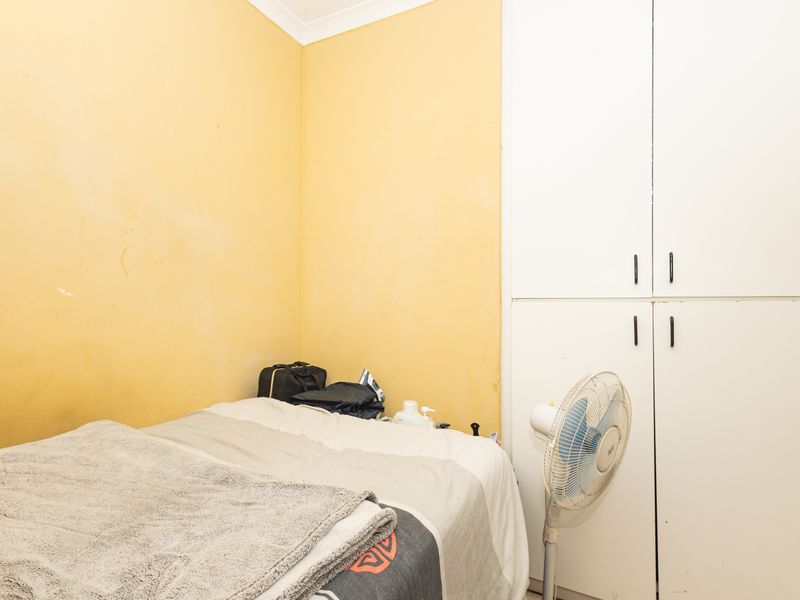 A compact bedroom featuring a built-in wardrobe and yellow painted walls, requiring cosmetic updates to improve the overall aesthetic.