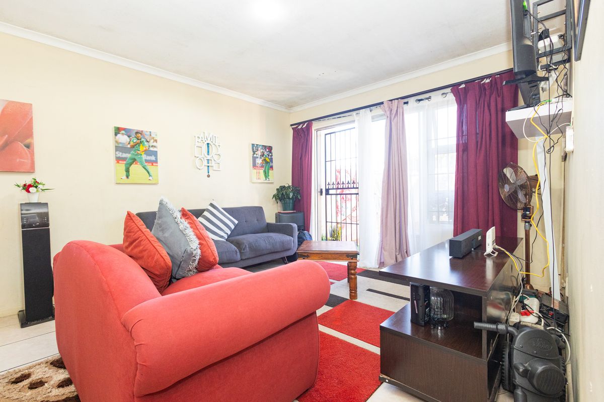 A living room featuring tiled flooring, coved ceilings, and a sliding glass door with an integrated security gate providing access to the exterior.