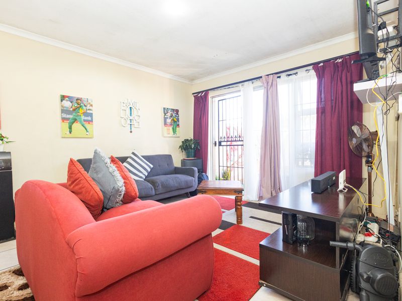 A living room featuring tiled flooring, coved ceilings, and a sliding glass door with an integrated security gate providing access to the exterior.