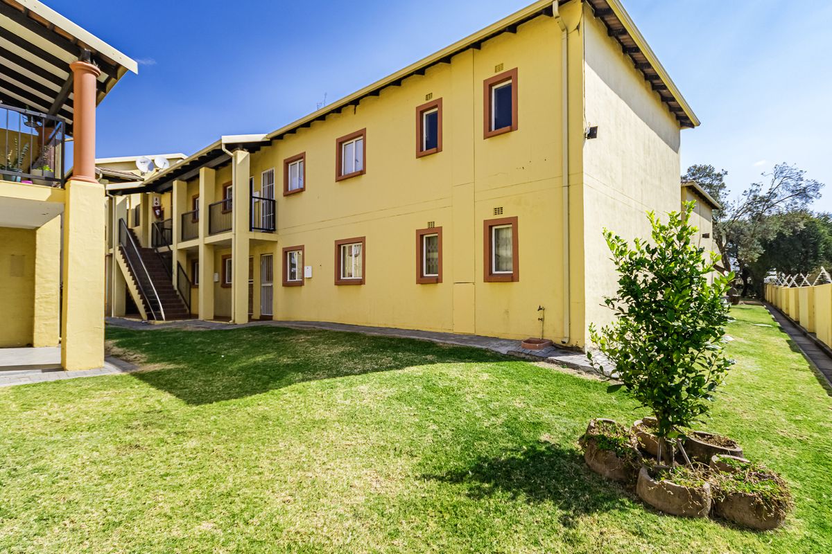 Rear view of a multi-story apartment complex featuring exterior staircases, balconies, and a shared garden area with paved walkways.