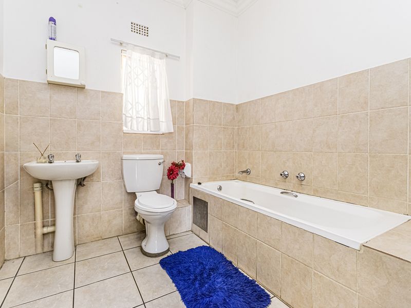 A functional bathroom featuring a pedestal basin, toilet, and a built-in bathtub with neutral ceramic wall and floor tiling.