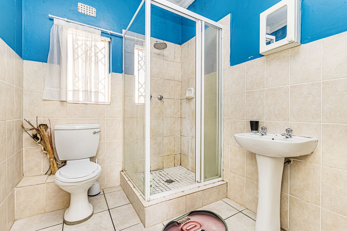 A functional bathroom featuring a shower enclosure, pedestal basin, and toilet, with tiled finishes and blue painted upper walls.