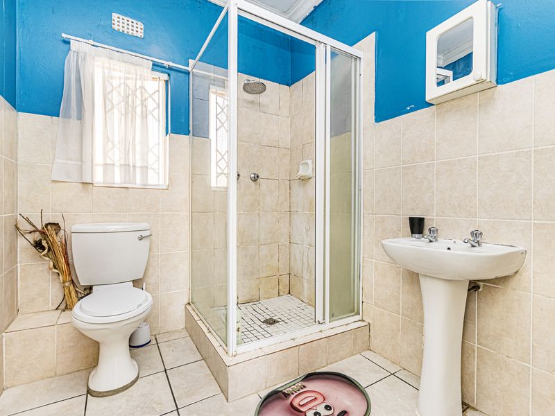 A functional bathroom featuring a shower enclosure, pedestal basin, and toilet, with tiled finishes and blue painted upper walls.