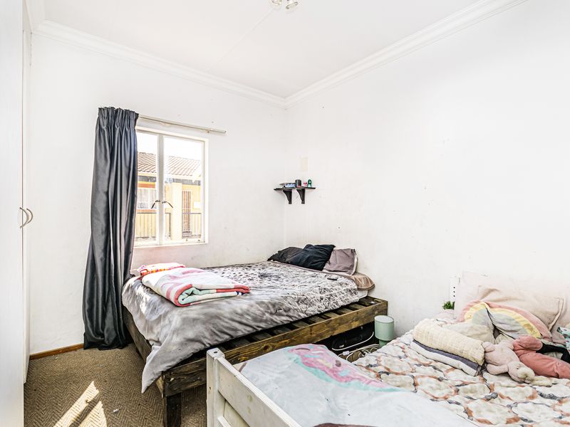 A bedroom featuring a built-in wardrobe, cornice detailing, and a window, currently showing signs of wear on the walls and flooring.