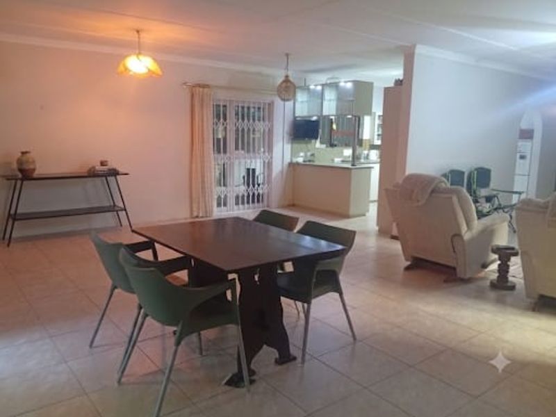 Spacious open-plan living and dining area featuring tiled flooring, flowing into a functional kitchen with built-in cabinetry and a breakfast bar.