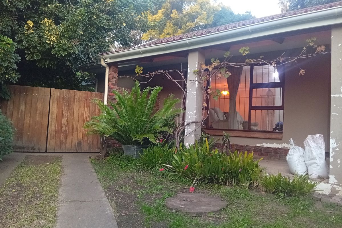 Rear exterior view of the house featuring a covered patio, brick pillars, and a garden pathway with a wooden gate.