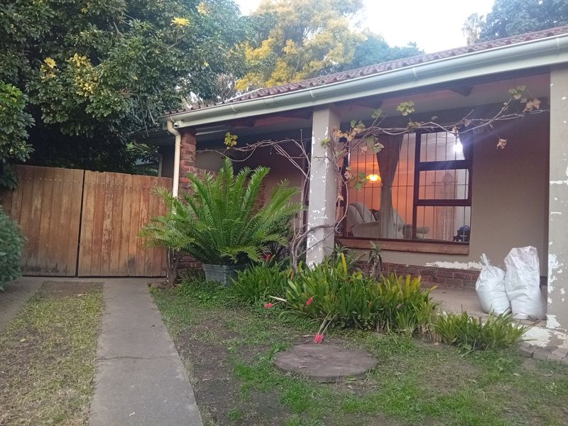 Rear exterior view of the house featuring a covered patio, brick pillars, and a garden pathway with a wooden gate.