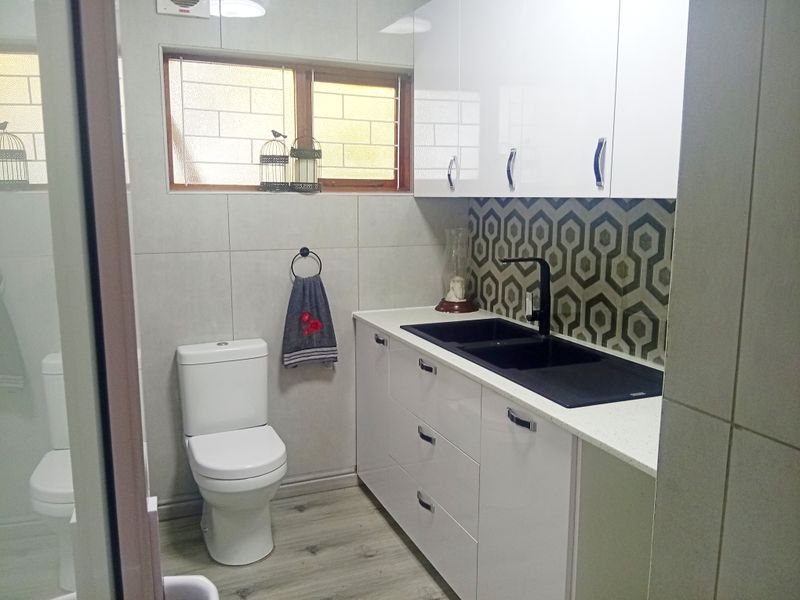 Modern bathroom featuring white gloss cabinetry, stone countertops, a black double basin sink, and a stylish geometric patterned splashback.