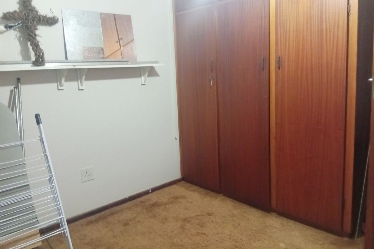 A bedroom featuring built-in wooden cupboards and a wall-mounted shelf, with carpeted flooring throughout.