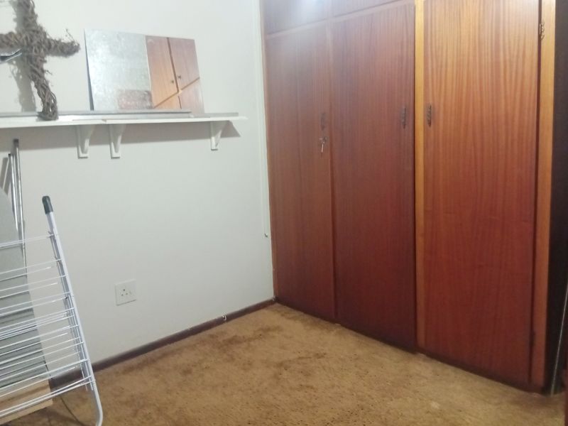 A bedroom featuring built-in wooden cupboards and a wall-mounted shelf, with carpeted flooring throughout.
