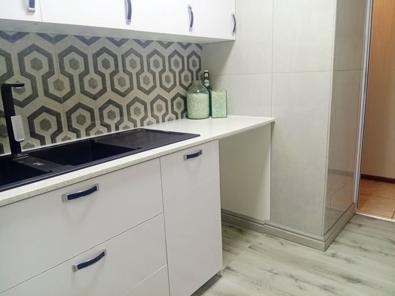 A modern, clean kitchen area featuring white cabinetry, a geometric tile splashback, and a black sink with a matching mixer tap.