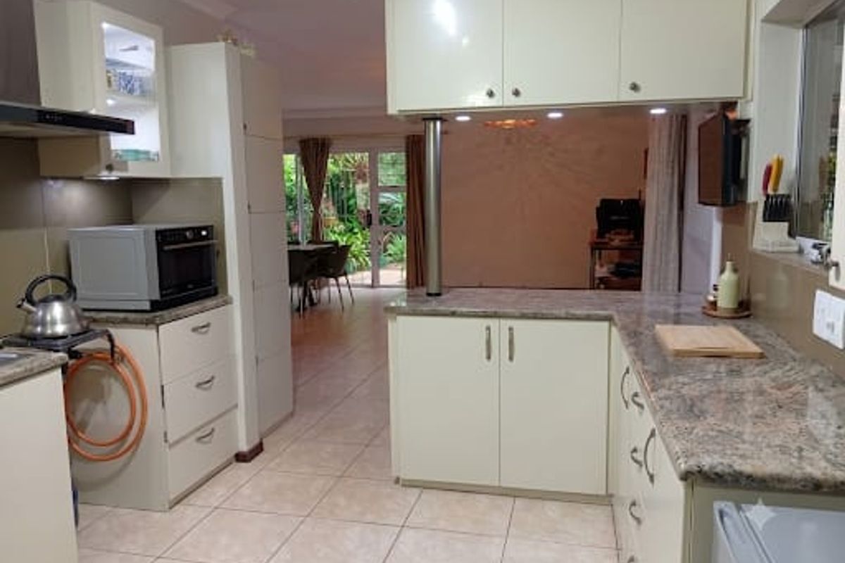 A functional kitchen featuring granite countertops, ample built-in cabinetry, and an extractor fan, with an open-plan layout flowing into the adjacent living area.