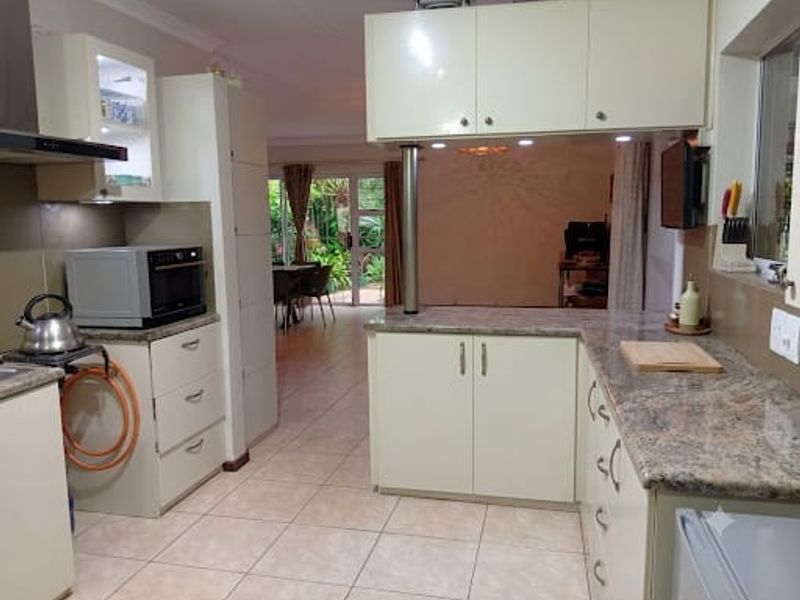 A functional kitchen featuring granite countertops, ample built-in cabinetry, and an extractor fan, with an open-plan layout flowing into the adjacent living area.