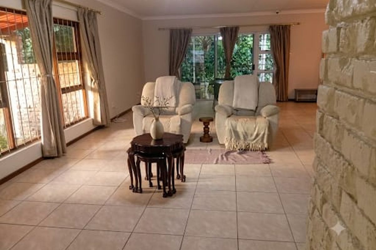 Spacious living area featuring neutral tiled flooring, an exposed brick feature wall, and large sliding glass doors providing access to the garden.