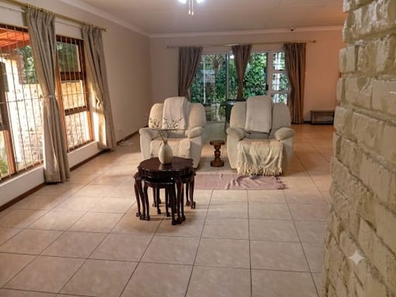 Spacious living area featuring neutral tiled flooring, an exposed brick feature wall, and large sliding glass doors providing access to the garden.