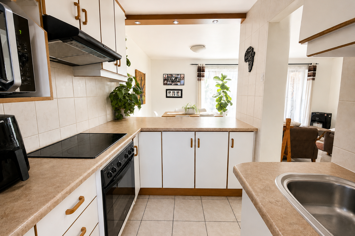 A functional kitchen featuring built-in cabinetry, laminate countertops, a tiled splashback, and integrated appliances, flowing into an adjacent dining and living area.