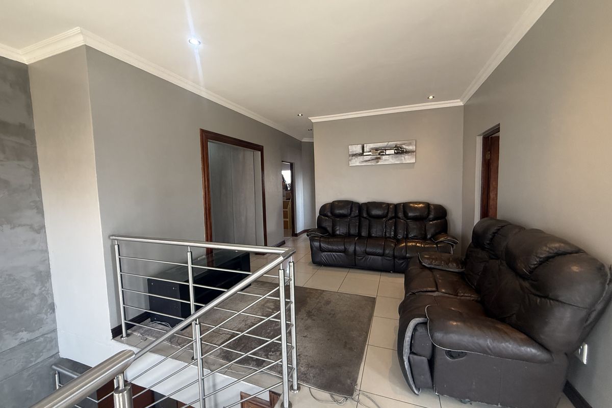 A spacious living area featuring tiled flooring, recessed downlighting, and a modern stainless steel balustrade overlooking the staircase.