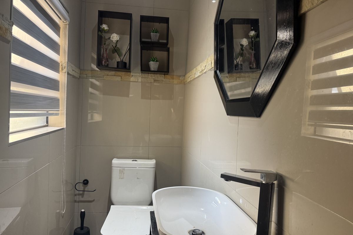 A compact, modern bathroom featuring tiled walls, a vessel sink with a contemporary faucet, and a wall-mounted mirror.