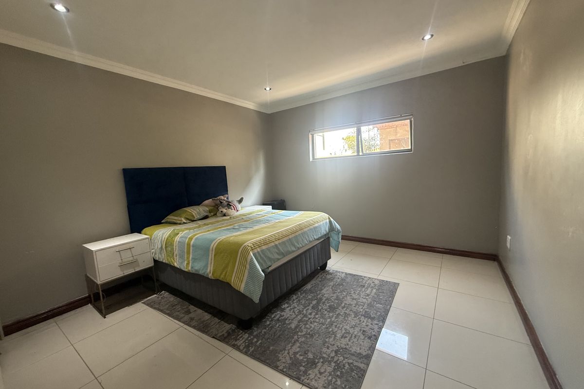 A spacious bedroom featuring neutral wall tones, tiled flooring, recessed downlighting, and a high-level window providing natural light.
