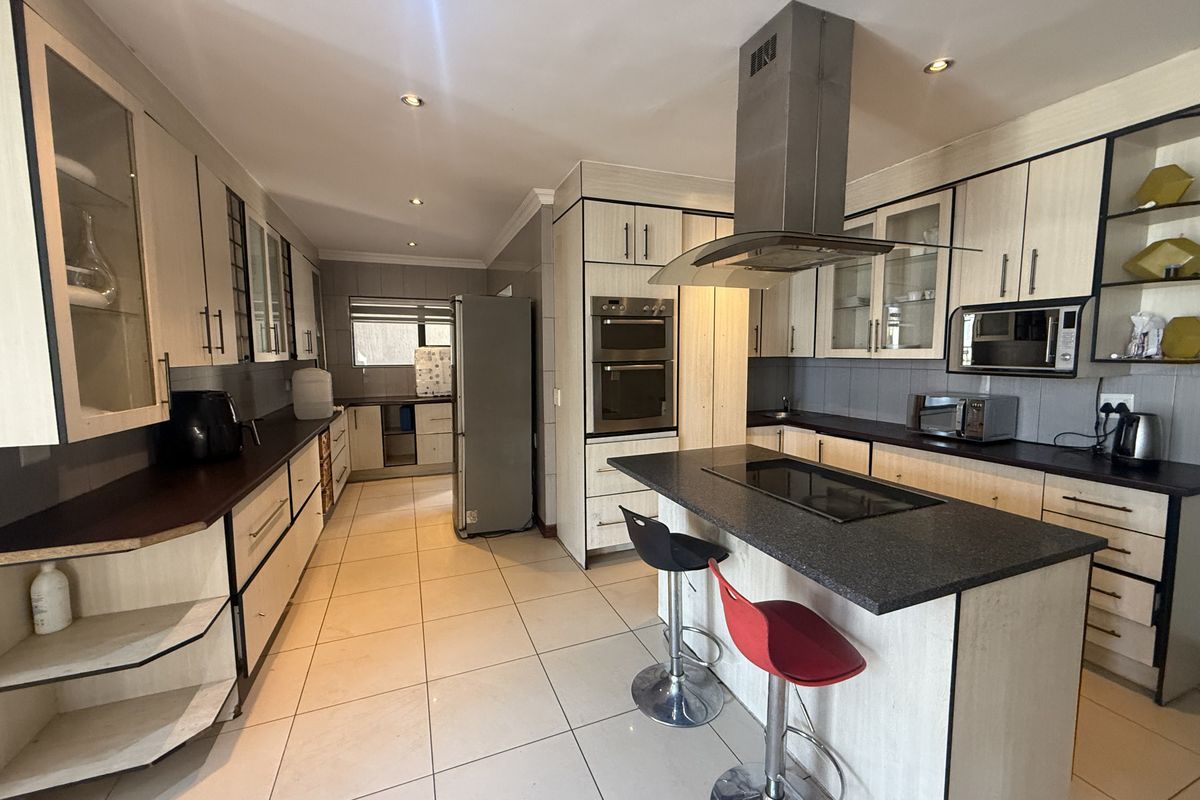 Spacious kitchen featuring modern cabinetry, a central island with a built-in hob, integrated appliances, and tiled flooring throughout.