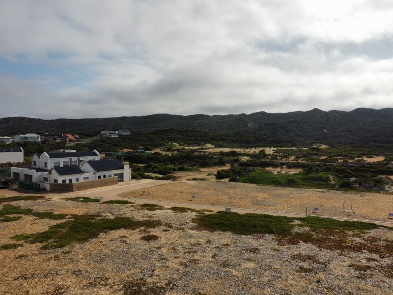 An aerial view of a vacant residential plot featuring natural coastal vegetation and access to a paved road in a scenic landscape.