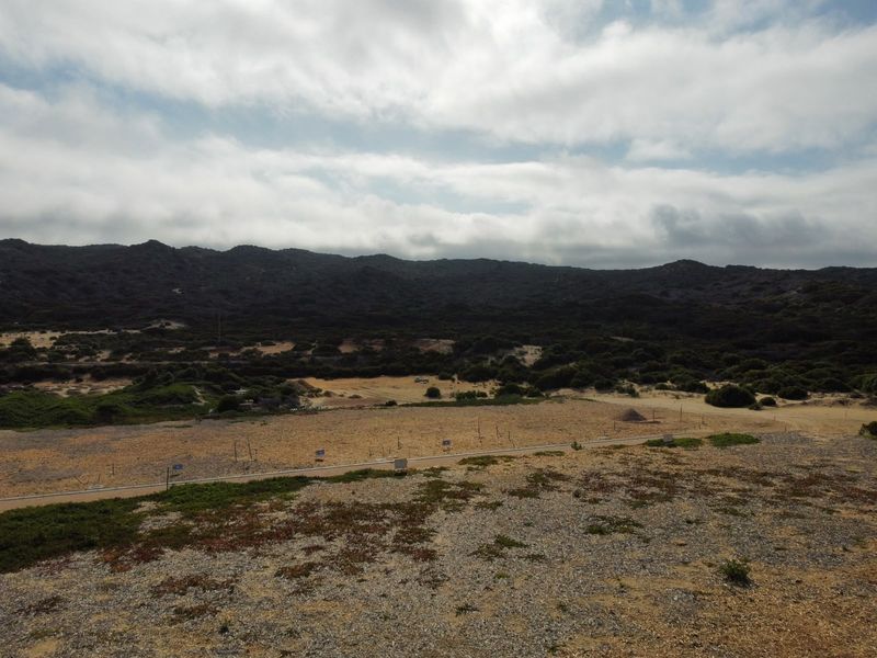 An aerial view of a large, undeveloped residential land plot featuring natural vegetation and surrounding mountain landscape.