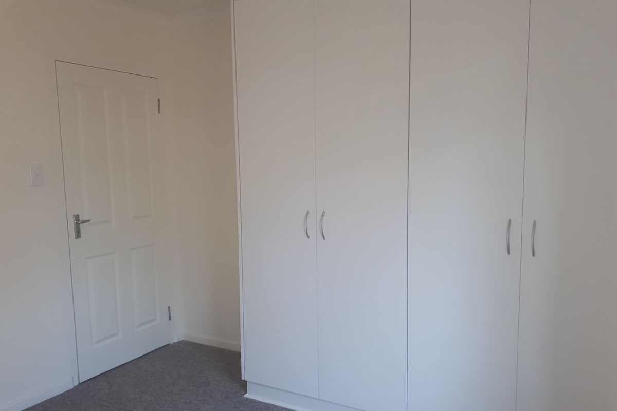 A clean, neutral bedroom featuring built-in white wardrobes and carpeted flooring, offering a blank canvas for personalization.