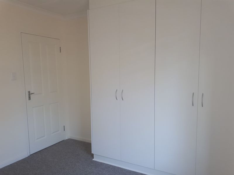 A clean, neutral bedroom featuring built-in white wardrobes and carpeted flooring, offering a blank canvas for personalization.