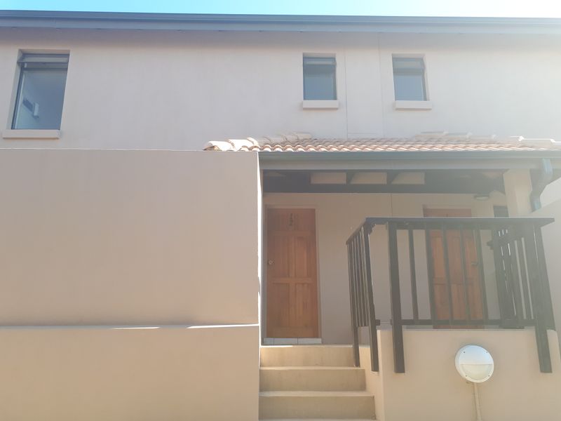 Front elevation of an apartment unit featuring timber entrance doors, concrete stairs with balustrade, and terracotta roof tiling.