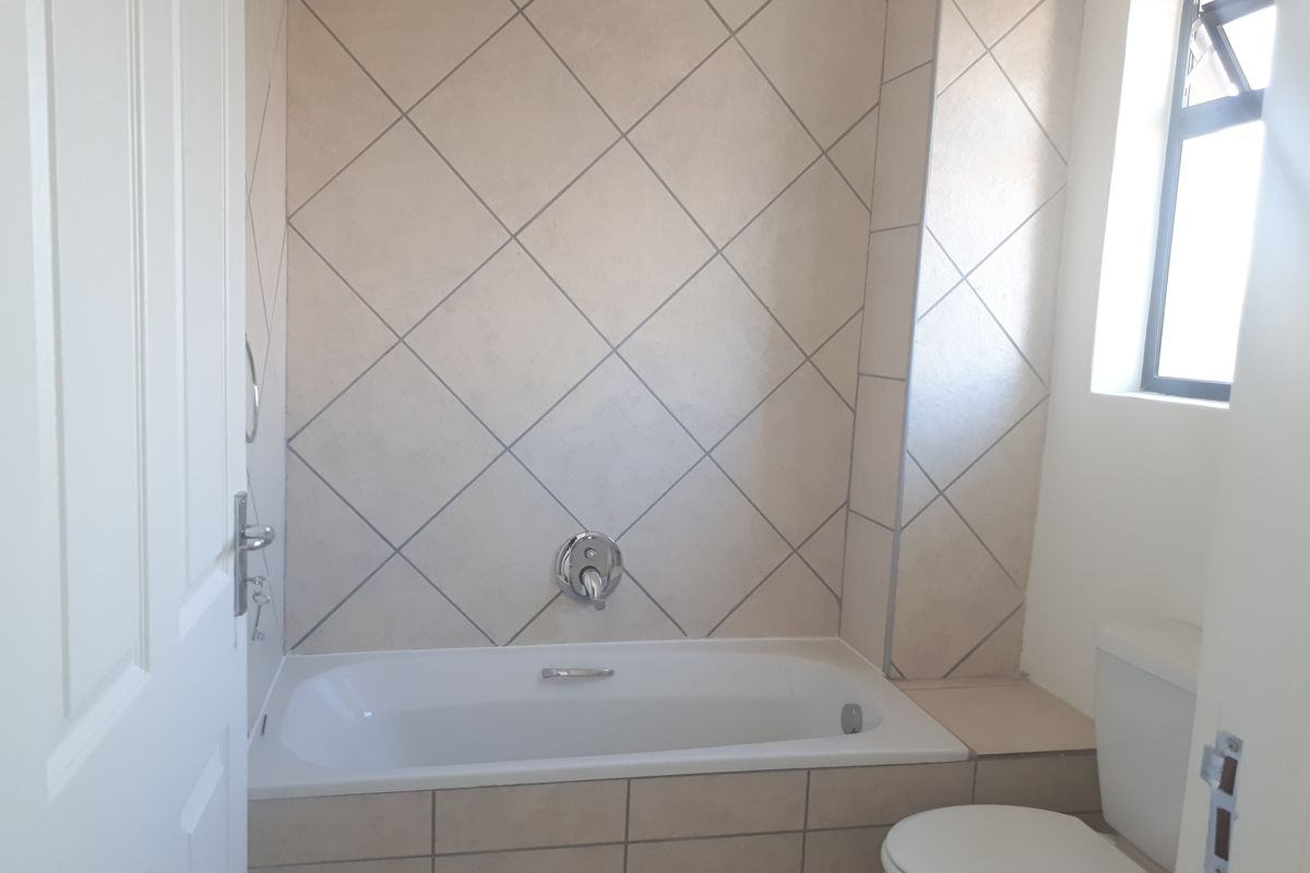A functional bathroom featuring a built-in bathtub with wall-mounted shower head, tiled splashback, and a standard toilet.