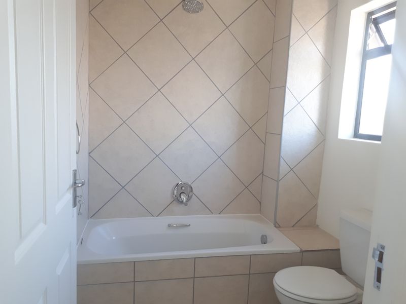A functional bathroom featuring a built-in bathtub with wall-mounted shower head, tiled splashback, and a standard toilet.