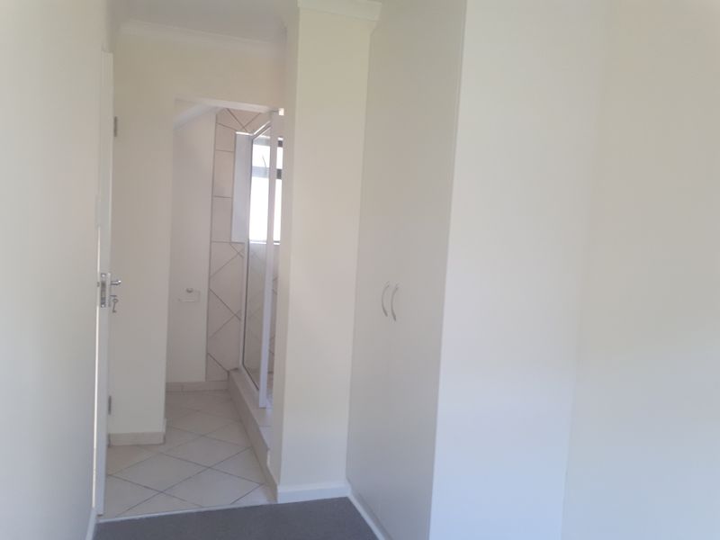 A clean, neutral hallway featuring built-in storage cupboards and direct access to an adjacent tiled bathroom with a shower enclosure.