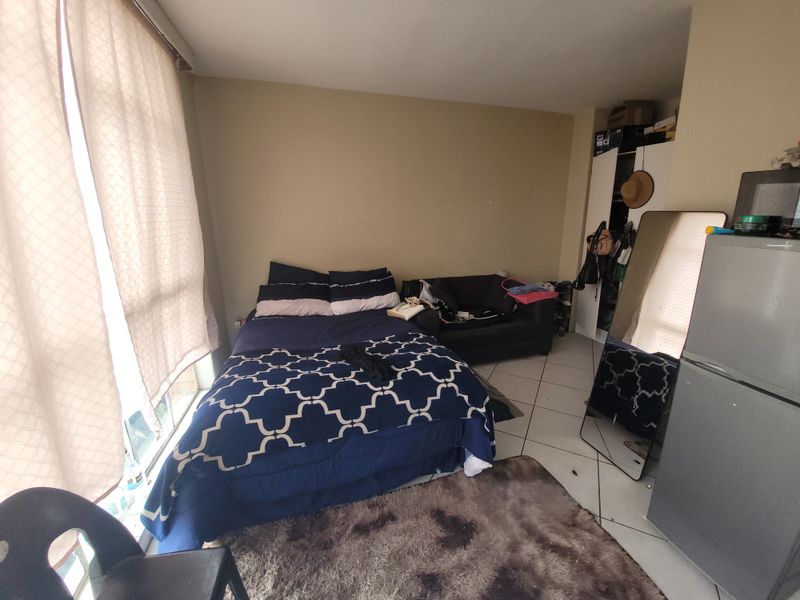 A bedroom featuring tiled flooring and a built-in cupboard, offering a functional living space with natural light from the adjacent window.