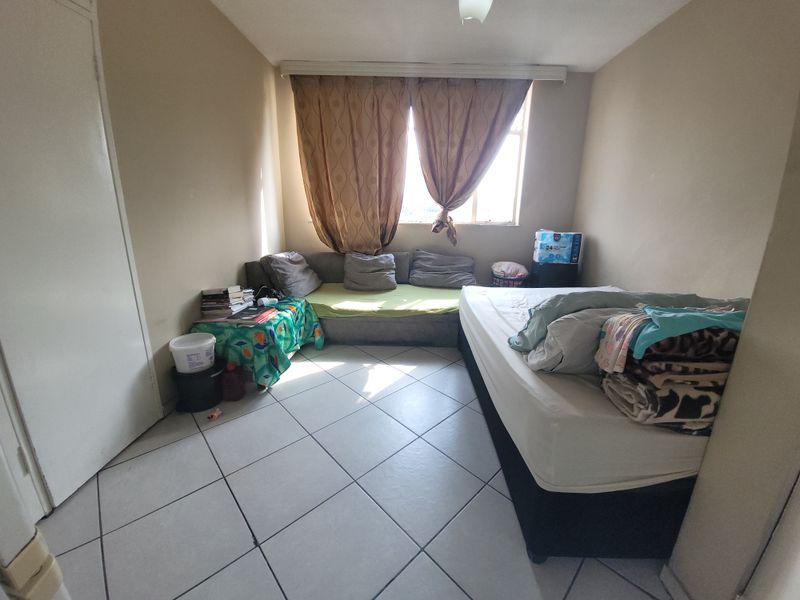 A bedroom featuring tiled flooring and a window with a curtain rail, offering a functional space ready for cosmetic updates and modernization.