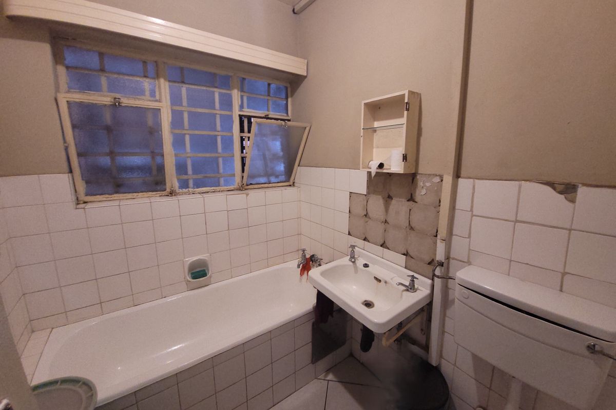 A dated bathroom featuring a bathtub, wall-mounted basin, and toilet, currently requiring significant renovation and repair to the wall tiling and finishes.