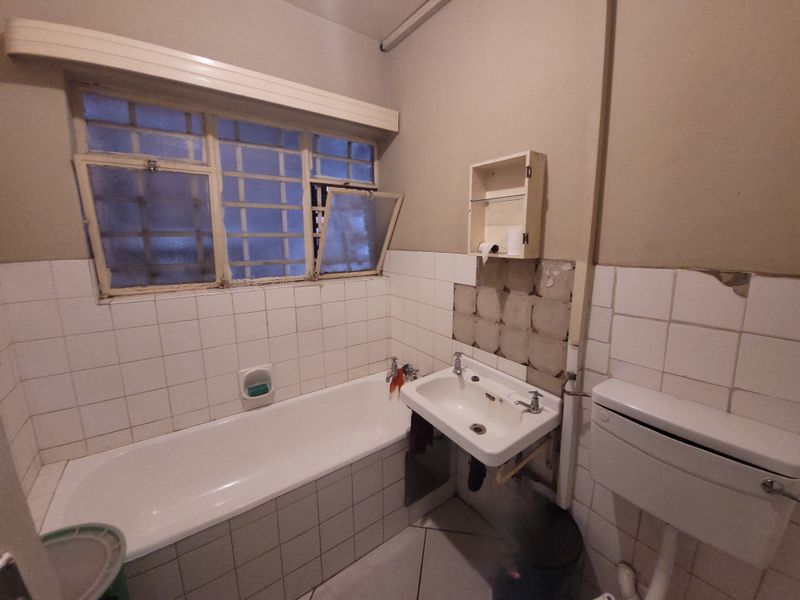 A dated bathroom featuring a bathtub, wall-mounted basin, and toilet, currently requiring significant renovation and repair to the wall tiling and finishes.