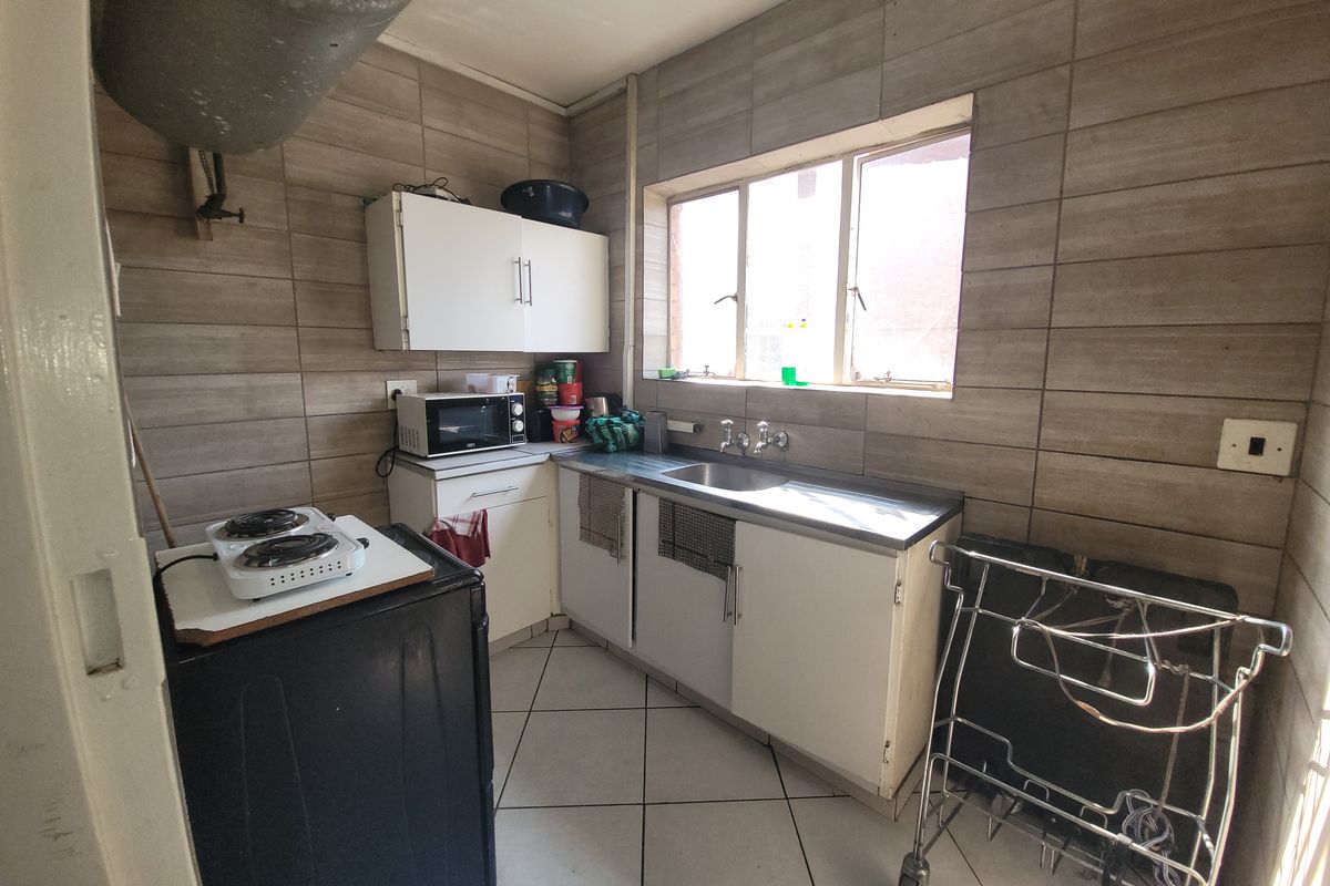 A compact kitchen featuring tiled walls and flooring, stainless steel sink, and built-in cabinetry, offering a functional space ready for modernization.